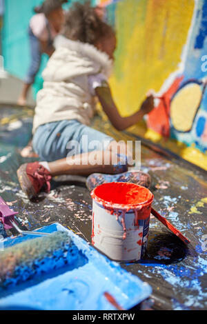Girl painting mural behind paint can Stock Photo