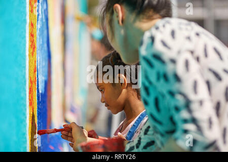 Teacher and elementary girl student painting on wall Stock Photo