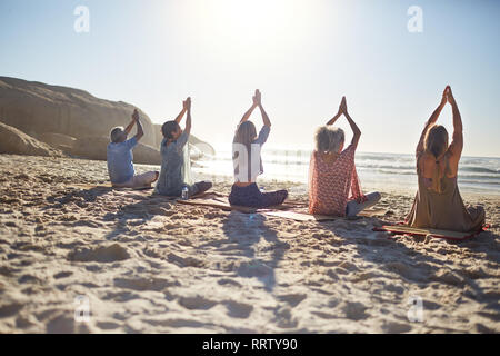 Group practicing yoga on sunny beach during yoga retreat Stock Photo