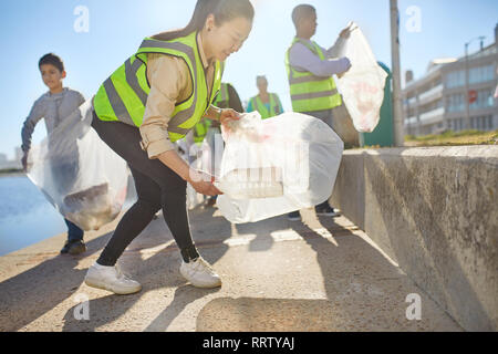 Woman volunteer picking up plastic litter on sunny boardwalk Stock Photo