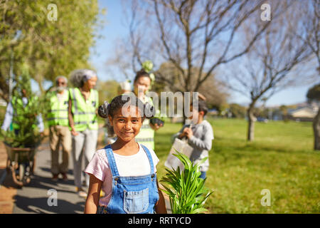 Portrait smiling, confident girl volunteering, planting trees in sunny park Stock Photo