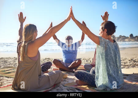 Group joining hands in circle on sunny beach during yoga retreat Stock Photo