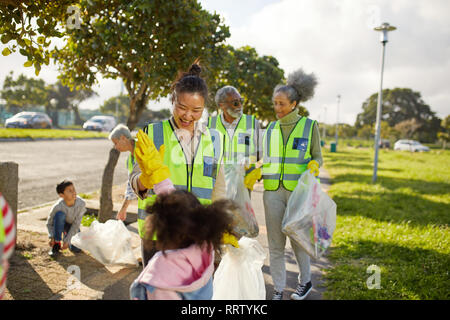 Happy volunteers high-fiving, cleaning up litter in sunny park Stock Photo