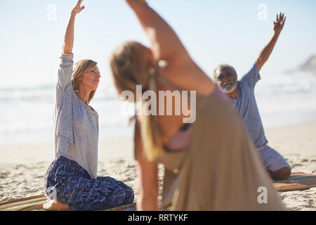 Group stretching on sunny beach during yoga retreat Stock Photo
