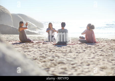 Group meditating in circle on sunny beach during yoga retreat Stock Photo