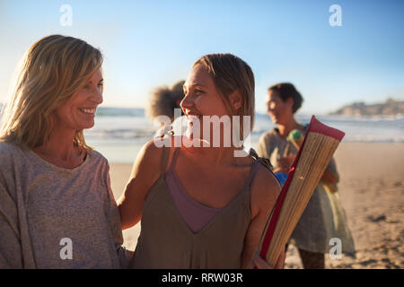 Happy mother and daughter with yoga mat on sunny beach during yoga retreat Stock Photo