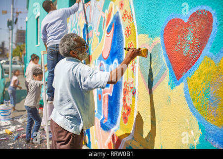 Senior man painting mural on sunny urban wall Stock Photo