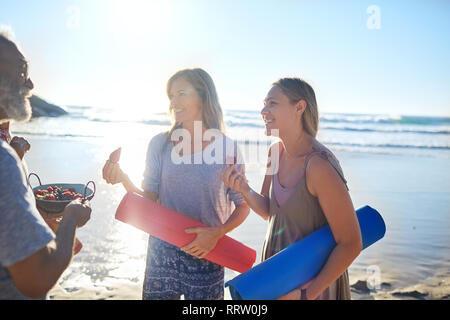 Mother and daughter with yoga mats eating fresh berries on sunny beach during yoga retreat Stock Photo