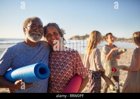 Portrait happy senior couple with yoga mats on sunny beach during yoga retreat Stock Photo