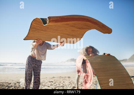 Woman laying yoga mats on sunny beach during yoga retreat Stock Photo