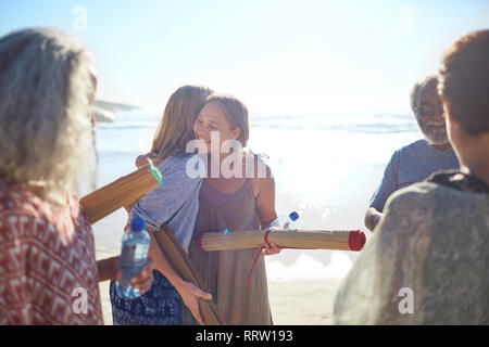 Women friends with yoga mats hugging on sunny beach during yoga retreat Stock Photo