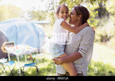 Portrait affectionate mother and daughter hugging at sunny campsite Stock Photo