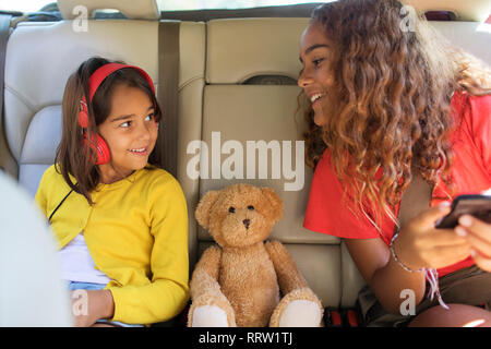 Sisters and teddy bear riding in back set of car Stock Photo