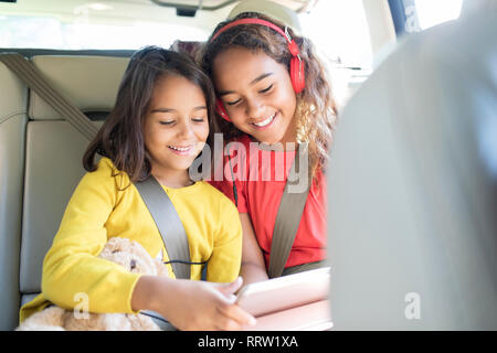 Sisters using digital tablet in back set of car Stock Photo