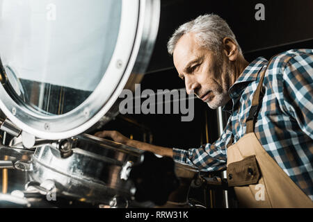 senior brewer in working overalls checking brewery equipment