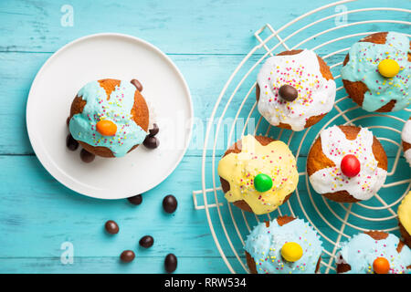 Easter or birthday cupcakes glazed with colorful sugar, sprinkles and chocolate for a kids party on a cooling rack on a turquoise wooden background. T Stock Photo