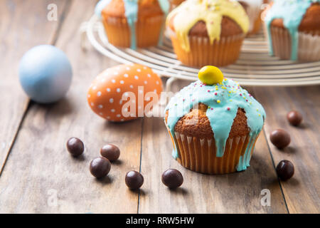 Easter cupcakes glazed with colorful sugar, sprinkles and chocolate and painted eggs on a rustic wooden table Stock Photo