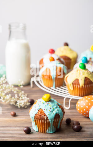 Easter cupcakes glazed with colorful sugar, sprinkles and chocolate with a bottle of milk and painted easter eggs  on a rustic wooden table Stock Photo