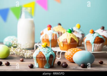 Easter cupcakes glazed with colorful sugar, sprinkles and chocolate with a bottle of milk and painted easter eggs  on a rustic wooden table against a  Stock Photo