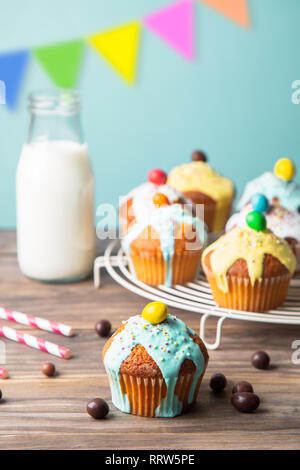 Easter or birthday cupcakes glazed with colorful sugar, sprinkles and chocolate with a bottle of milk  on a rustic wooden table against a turquoise ba Stock Photo