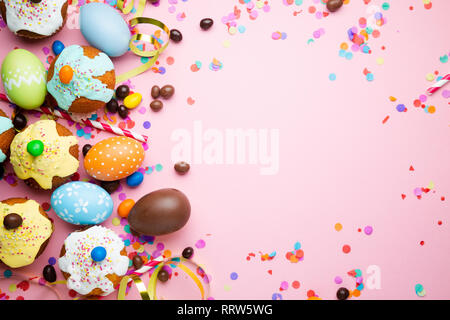 Easter party concept with easter eggs, cupcakes, chocolate, candies, confetti on a pink packground. Top view, copy space Stock Photo