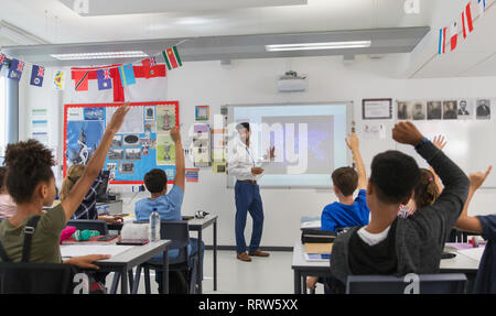 Junior high school students raising hands for teacher leading lesson in classroom Stock Photo