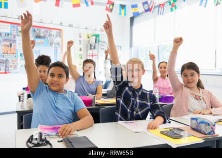 Eager junior high school students with hands raised in classroom Stock Photo
