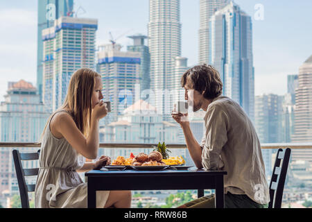 Loving couple having breakfast on the balcony. Breakfast table with coffee fruit and bread croisant on a balcony against the backdrop of the big city Stock Photo