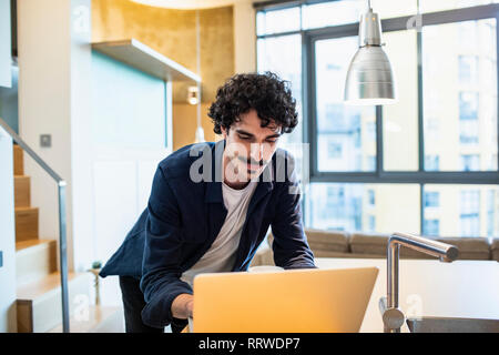 Man using laptop in apartment kitchen Stock Photo