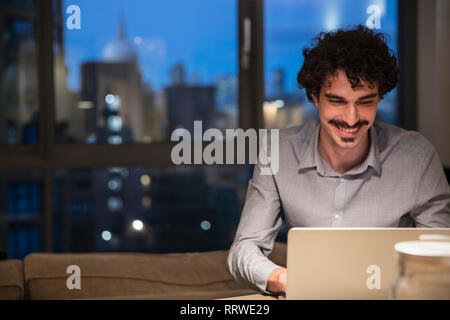 Man using laptop in urban apartment at night Stock Photo