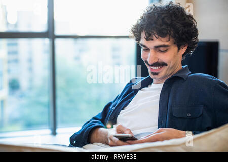 Smiling man using smart phone on sofa Stock Photo