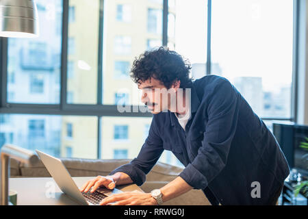Focused man using laptop in urban apartment kitchen Stock Photo