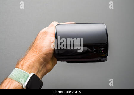 Patient holding against gray background modern electronic internet connected wireless upper arm blood pressure monitor front view  Stock Photo
