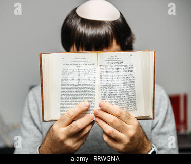 Young Jewish male wearing Kippah praying reading Bi-lingual Hebrew French mahzor prayer book from 1920 used on the High Holy Days of Rosh Hashanah and Yom Kippur text in front. Stock Photo