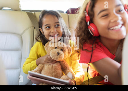 Happy sisters with teddy bear riding in back seat of car Stock Photo
