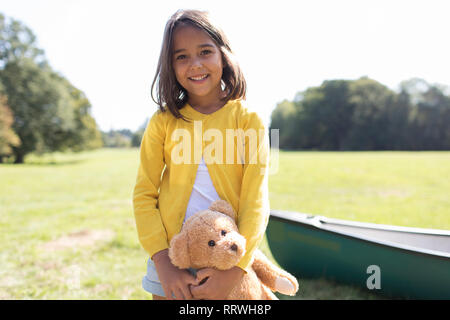 Portrait smiling, cute girl with teddy bear in sunny field Stock Photo