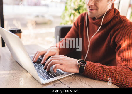 cropped view of man listening music in earphones while using laptop in cafe Stock Photo
