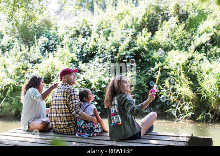 Family blowing bubbles on dock in woods Stock Photo