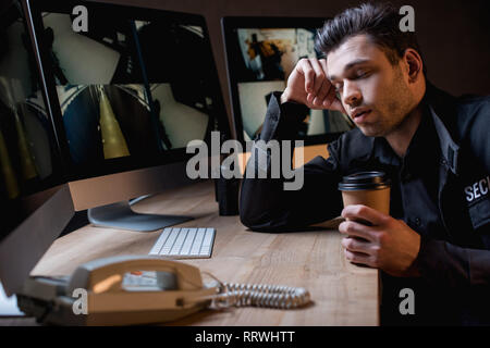 guard holding paper cup and sleeping in uniform at workplace Stock Photo