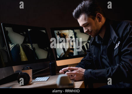 smiling guard in uniform using smartphone at workplace Stock Photo