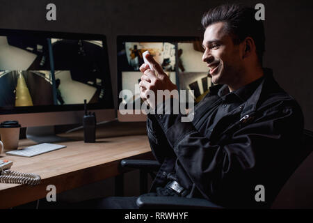 smiling guard in uniform using smartphone at workplace Stock Photo