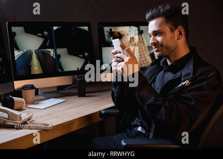 smiling guard in uniform using smartphone at workspace Stock Photo
