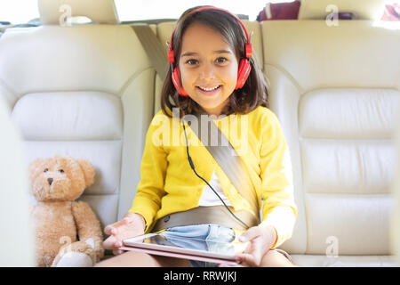 Portrait smiling, confident girl watching movie with headphones and digital tablet in back seat of car Stock Photo