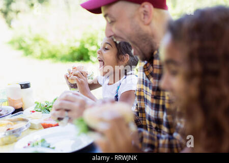 Playful father and daughter eating barbecue hamburgers at campsite Stock Photo