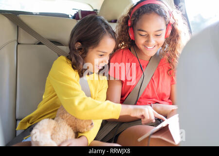 Sisters using digital tablet in back seat of car Stock Photo