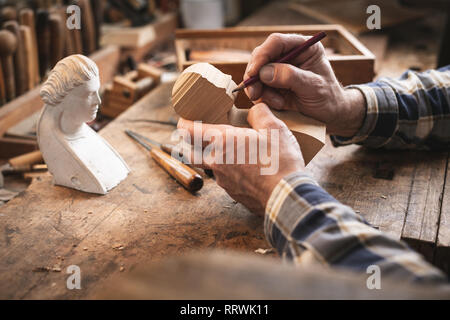 Experienced hands of an artisan sketching the outlines of a sculpture with a pencil Stock Photo