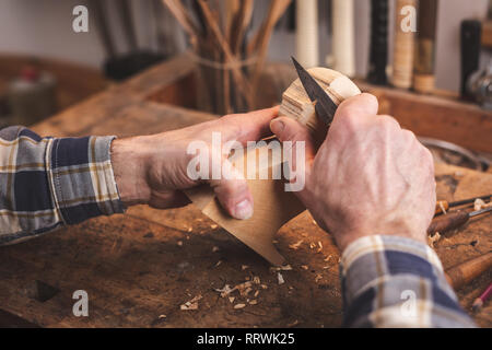 Hands of a man using a knife to carve a small piece of wood on a workbench Stock Photo