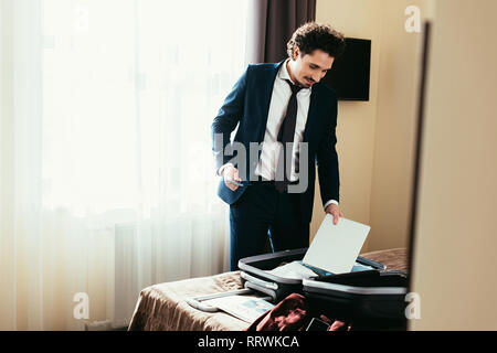 adult businessman putting laptop into suitcase on bed in hotel room Stock Photo