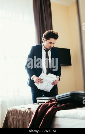 adult businessman putting clothes in suitcase on bed in hotel room Stock Photo