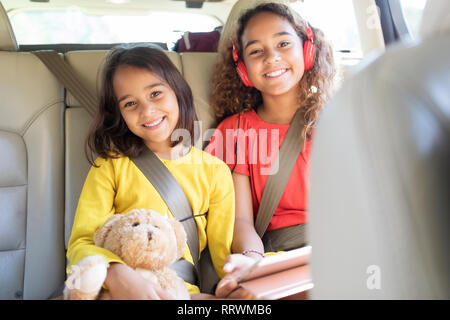 Portrait happy sisters with teddy bear riding in back seat of car Stock Photo